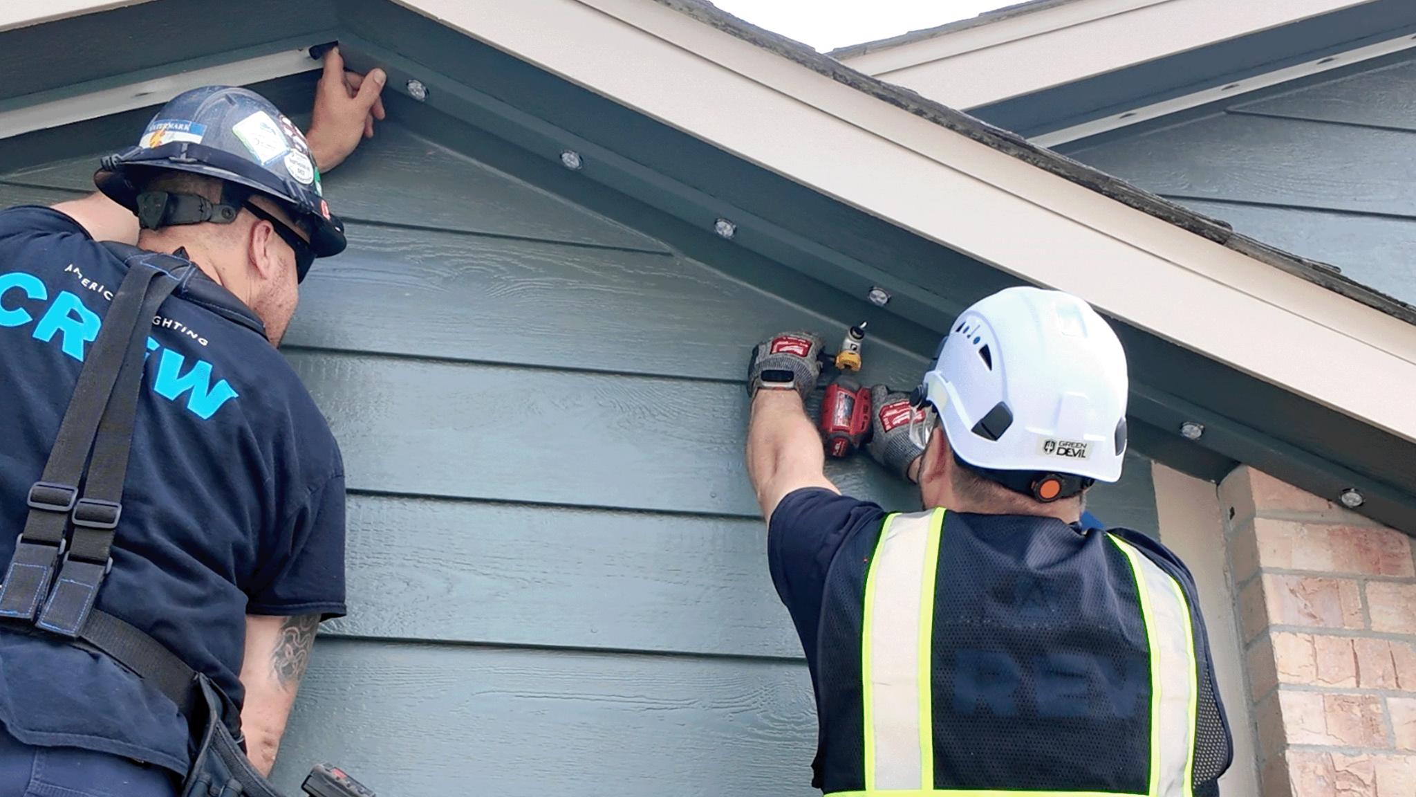 Professional crew installing low-profile permanent lighting beneath the eaves of a Charlotte home